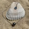 Bracelet chaîne fine argenté sur le sable avec un coquillage