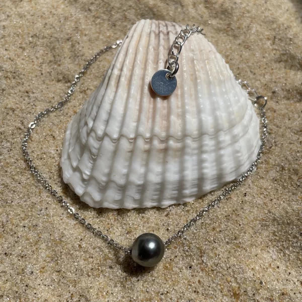 Bracelet chaîne fine argenté sur le sable avec un coquillage